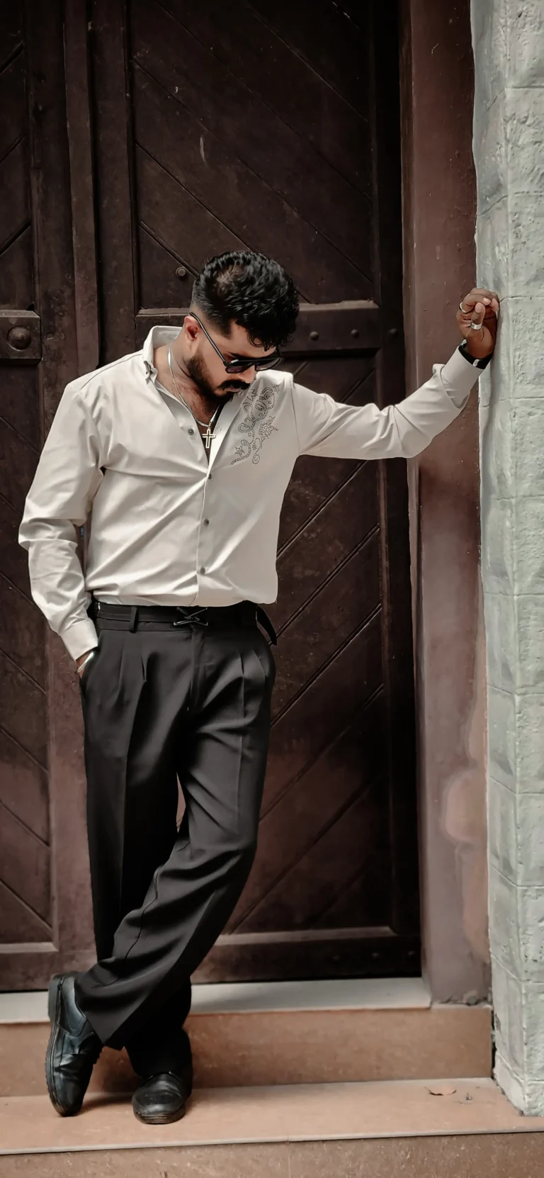 alt="Digital marketer in professional attire posing by a rustic wooden door.''
